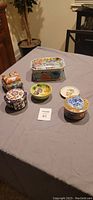 Five Japanese ceramic decorative boxes and small plates arranged on a grey cloth surface.