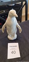 Front view of white ceramic penguin figurine on black surface with MaxSold tag