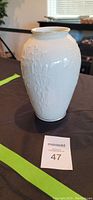 White Lenox vase with embossed floral design and gold rim on a black surface.