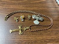 All items displayed together on wood surface: a large gold-tone cross pendant necklace and four assorted figurine and angel pins.