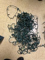 Tangled green wired Christmas lights on floor showing many small bulbs in a cluster.