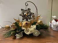 Full view of the holiday centerpiece on a wooden table with gold and green decorations and hanging glass star lantern.