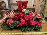 Front angle of Christmas centerpiece showing red glass vase, poinsettias, ribbon, ornaments, and gold birds