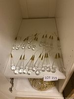 Multiple clear teardrop-shaped glass Christmas ornaments with gold hanging strings arranged on a shelf.