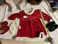 Red velvet doll dress with white faux fur trim and silver dots, laid flat with measuring tape showing length approx. 14 inches; includes white lace-trimmed socks and red doll shoes