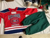 Red Montreal Canadiens hockey jersey paired with green doll pants laid flat.