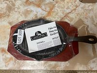 Cast iron grill pan resting on wooden serving board, showing lot number and GrillPro label