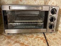 Front view of Hamilton Beach stainless steel toaster oven on countertop, showing glass door and interior wire rack with baking tray.