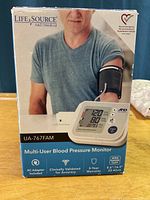 Box showing Life Source A&D Medical UA-767FAM blood pressure monitor packaging with info and device usage image.