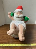 Front view of plush Santa with red hat and white textured suit, sitting upright with arms raised, holding green objects, approximate height 11 inches.