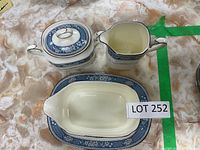 Photo of Noritake Bone China Randolph pattern covered sugar bowl, creamer, and gravy boat with stand on a textured beige surface.