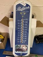 Full view of the blue and white thermometer with Packard Motor Cars logo and classic car image, showing thermometer scale and mercury tube.