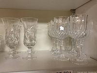 Photo of 2 pairs of Pinwheel pattern stemmed glasses and a group of Crystal D'Arques cut crystal stem glasses on a shelf.
