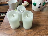 Three white flameless candles on wooden surface with other decorative items.