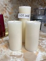 Three white pillar candles on a marble-patterned surface with kitchen appliances in the background.