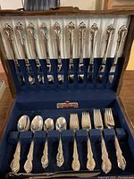 Full inside view of silverplated cutlery set in original wooden box with blue velvet lining showing knives in upper section and spoons and forks below.