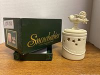 Photo of green Snowbabies box next to candle holder showing packaging and branding.