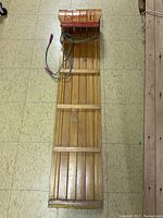 Full-length image of wooden Sno-Jet toboggan showing slat design and curved front with red Sno-Jet branding, attached pull rope visible.