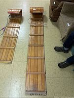 Top view showing the full length of the wooden toboggan laid out on the floor, highlighting the parallel slats and side rand.