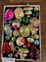 Full view of all vintage glass Christmas tree ornaments arranged in a box. Various shapes, sizes, and colors visible.