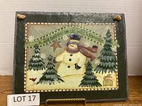Winter scene painting on slate including snowman, evergreen trees, bird, and bunny with text banner.