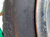 Snowflake symbol and "SAFETY WARNING" text on tire sidewall beside rusted steel rim