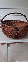 Side view of round antique woven basket displaying tight weave pattern and attached sturdy handle.