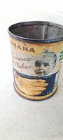 Side view of antique yellow and blue banana flakes baby food tin can showing lithographed baby image and bananas, illustrating condition and design.