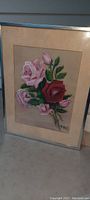 Full front view of the framed artwork showing a bouquet of red and pink roses with green leaves on beige paper, framed in a silver metal frame under glass.