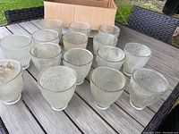 15 clear glass ribbed globes arranged on an outdoor wooden table with a cardboard box behind them.
