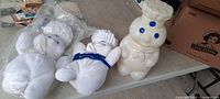 Three Pillsbury Doughboy items displayed on table: one blow mold plastic canister and two plush dolls.