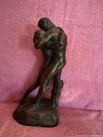 Front left angled view of resin bronze effect sculpture of embracing lovers on pink background