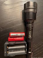 Photo of TrustFire flashlight, two rechargeable batteries, and travel charger on black surface.