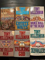 Top view of all six Tony Hillerman books neatly arranged flat on dark surface showing front covers: The Ghostway, Coyote Waits, Dance Hall of the Dead, The Fallen Man, Talking God, and Skinwalkers.