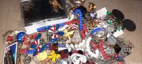 Photo showing a pile of colorful costume jewelry including necklaces with red, white, blue beads, Mickey Mouse pin, butterfly pins, and various other pins and chains.