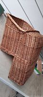 Side view of the woven wicker basket shaped to be a child seat, displaying the curved backrest and woven structure.