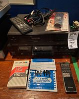 Full view showing Akai GX-R70EX stereo cassette deck stacked below Panasonic VHS Hi-Fi MTS player, remotes, RCA cables, sealed VHS tape, TDK cassette tape, and film developing packet.