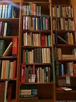 Tall bookshelf with multiple shelves housing a large collection of vintage books, hardbound mostly, some soft cover, various sizes and colors.