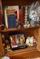 Wooden shelves containing blue, red, white taper candles, boxed and loose, with various tea light candles stacked in plastic containers, also pillar candles and boxed candles on bottom shelf