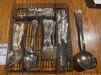 Overview of wire tray containing assorted forks, spoons, knives and one large ladle