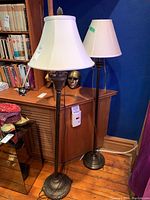 Two metal floor lamps side by side, one with basket-weave design, the other with fluted column and smaller shade.