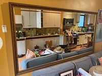 Full view of the large mirror hung over a couch reflecting a kitchen and the living area.