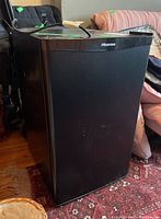 Front-side angle view of the black Hisense fridge showing minor surface scratches and its compact size.