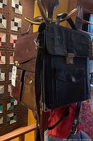 Photo showing two leather bags hanging, one black with multiple compartments and one dark brown with compartments.