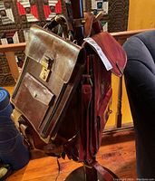 Three leather bags hanging on a wooden chair including the two shoulder bags and the satchel, showing overall condition and style.