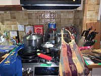 Kitchen stove area with multiple pans, pots, aprons, trays and tins visible.