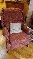 Front view of red patterned upholstered reclining chair with beige cushion on seat
