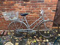 Side view of vintage Sekine cruiser bicycle with metal rear basket and flat tires, set against a brick wall.