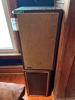 Two wood cabinet speakers stacked one on top of the other with brown woven cloth grills, showing ADC logo on bottom speaker.