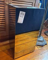 Front and side view of the mirrored cube stand showing reflective surfaces and wood floor reflection.